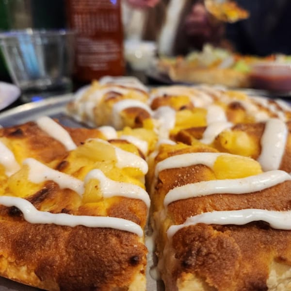 Close-up of a Tossers Pizza & Beer pineapple pizza with white sauce drizzled on top.