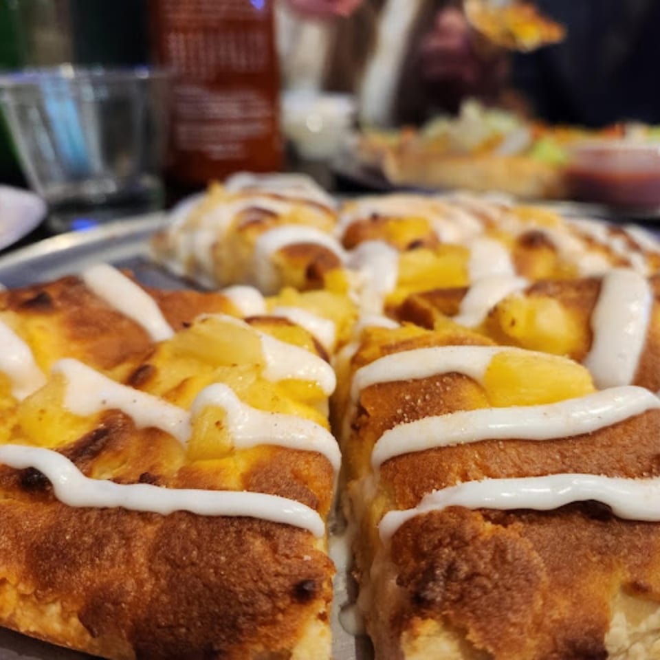 Close-up of a Tossers Pizza & Beer pineapple pizza with white sauce drizzled on top.
