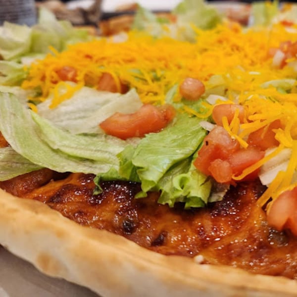 Close-up of a Tossers Pizza & Beer taco pizza with lettuce, tomatoes, and shredded cheese.