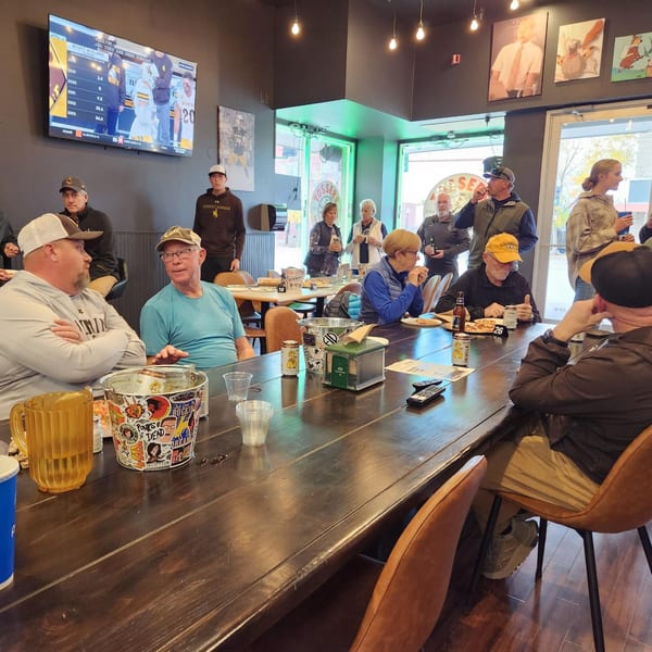 Patrons enjoying pizza and drinks at long wooden tables in Tossers Pizza & Beer, with a TV showing sports.