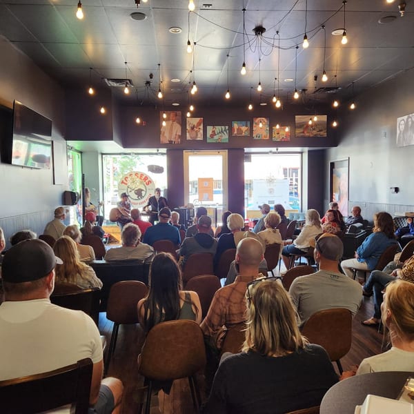 A crowd of people seated, watching a musical performance at Tossers Pizza & Beer.
