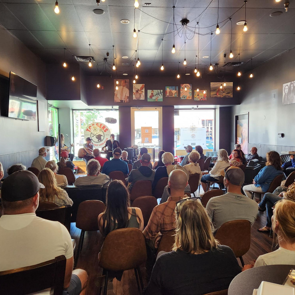 A crowd of people seated, watching a musical performance at Tossers Pizza & Beer.